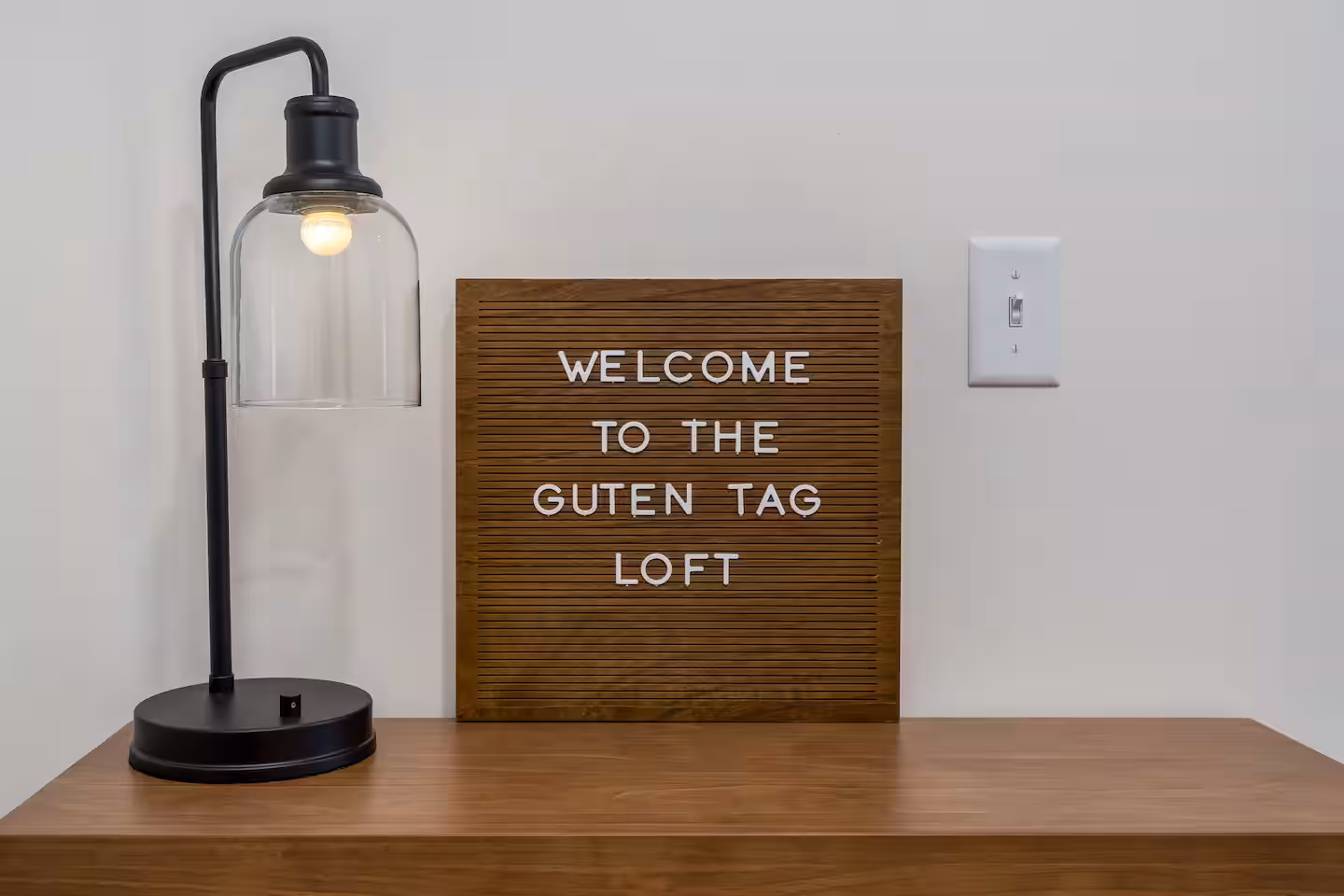 Welcome to the Guten Tag Loft Wood entry table with an industrial lamp and a letter board reading "Welcome to the Guten Tag Loft"