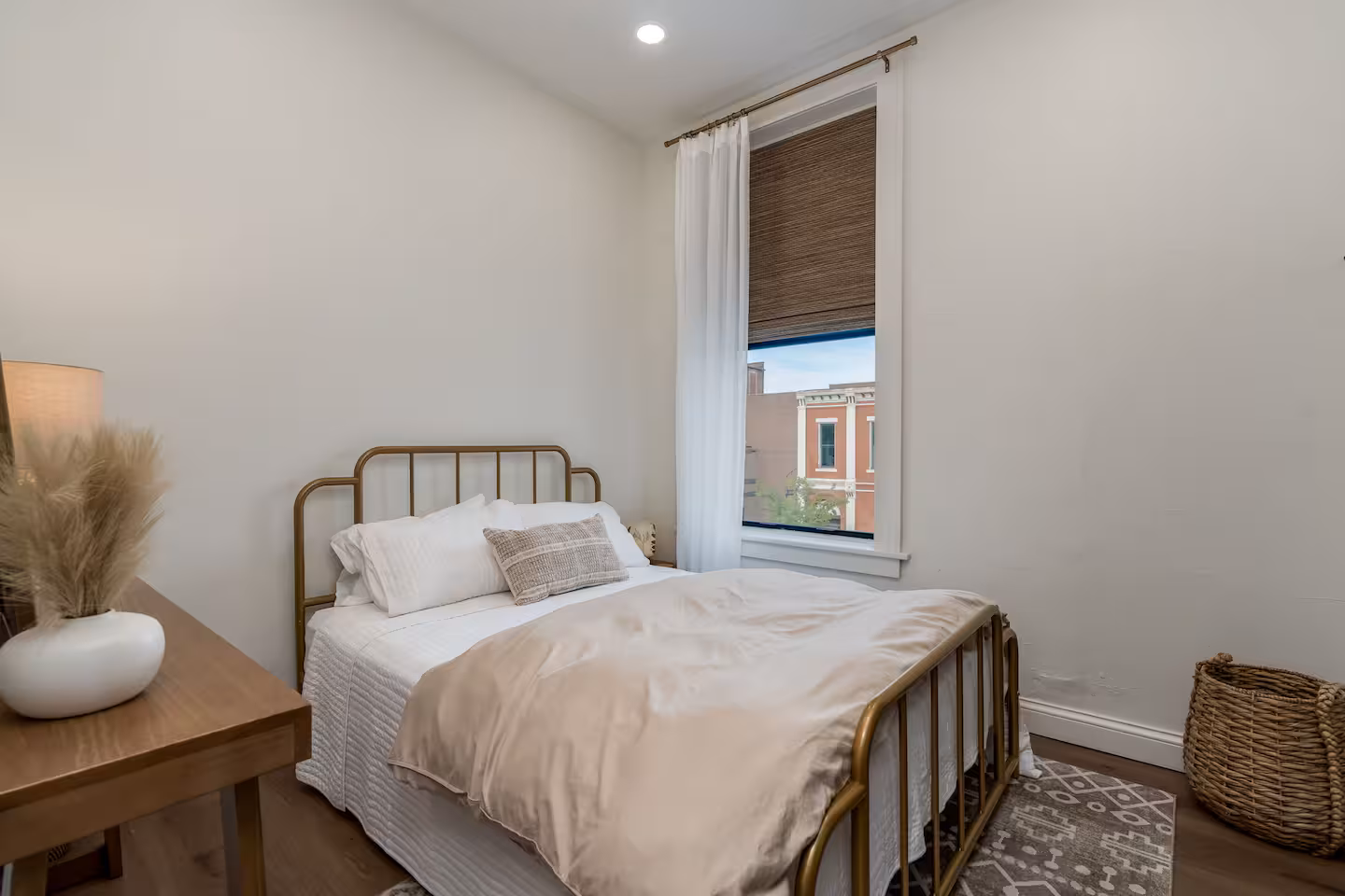Bedroom with Brass Bed Frame and City Window View Bedroom with brass metal bed frame, cream linens, and a window overlooking downtown New Ulm
