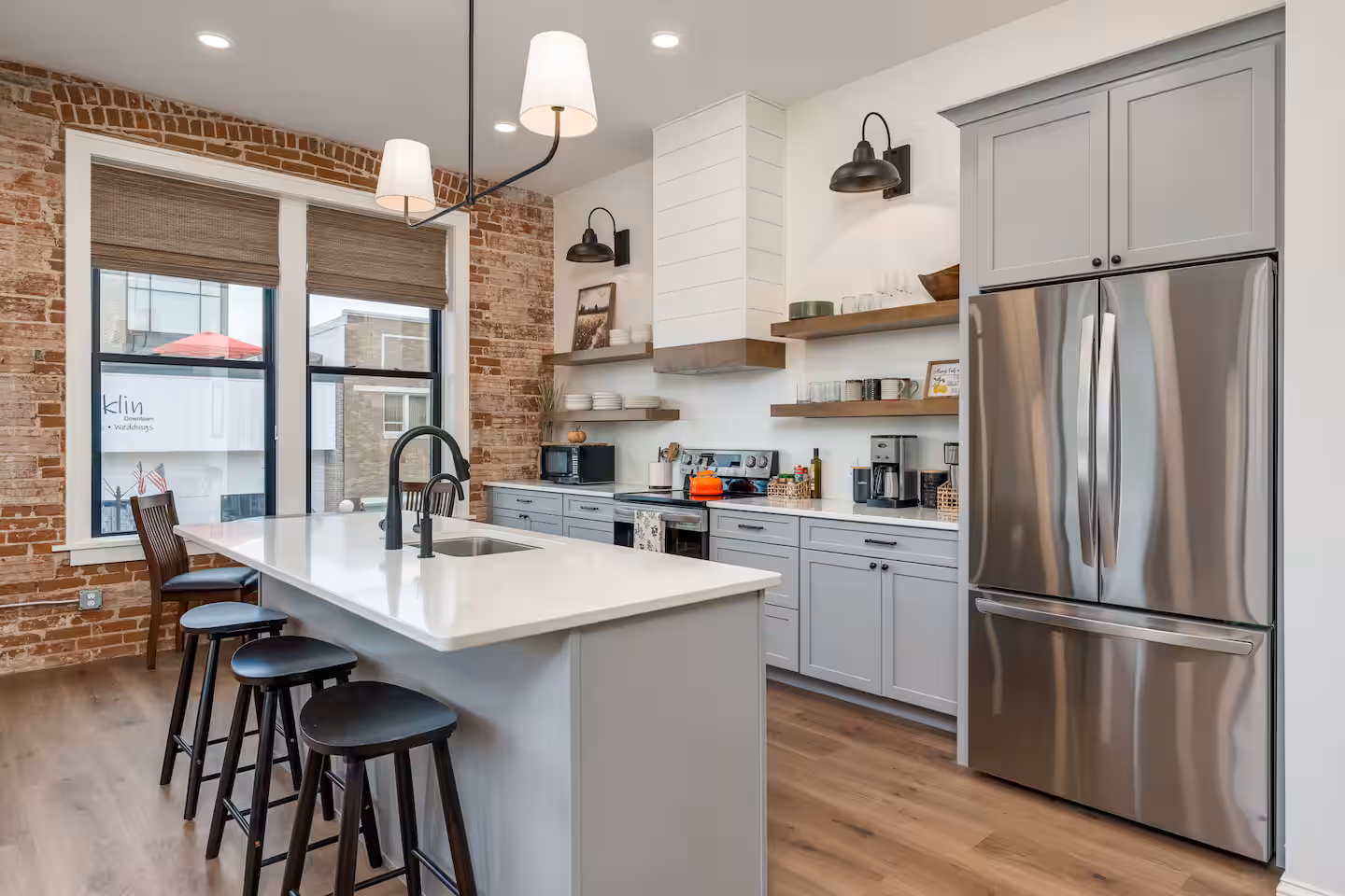 Kitchen with Gray Cabinetry and Quartz Island Living-Room3.avif — Living Room Seating Area with Downtown View Kitchen with gray cabinetry, white quartz island, stainless steel refrigerator, and brick accent wall