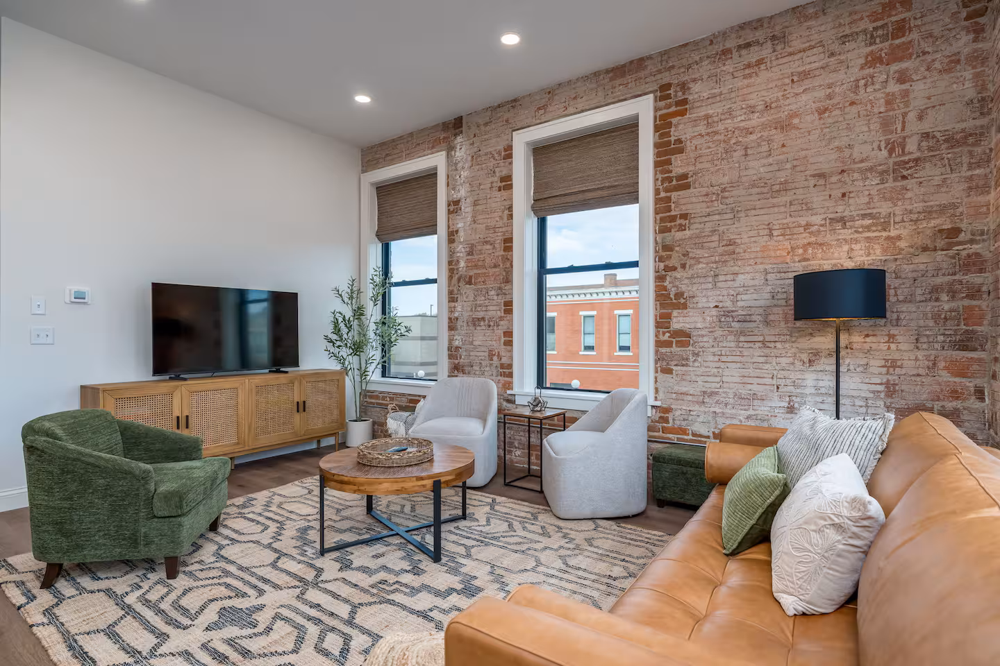 Living Room with Brick Accent Wall and TV Console Living room with exposed brick accent wall, wood media console, mounted TV, and cream and olive green accent chairs