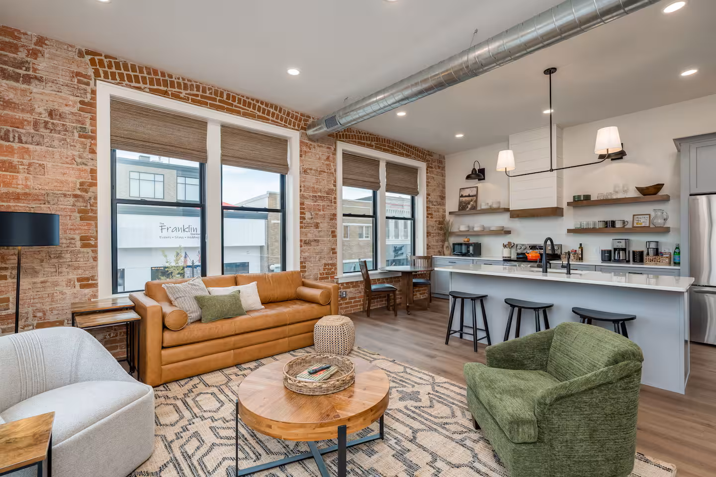 Living Room and Kitchen with Pendant Lighting Living room and kitchen with brick wall, leather sofa, round coffee table, and gray island with pendant lighting in the Guten Tag Loft